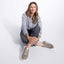 Woman sitting on a white floor wearing gray shoes, gray pants, and a light gray shirt.